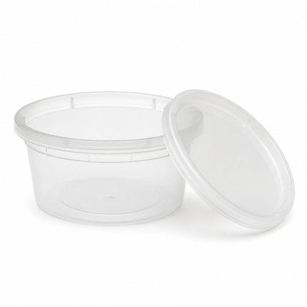 A clear plastic round food storage container with its matching lid leaning against it on a white background.