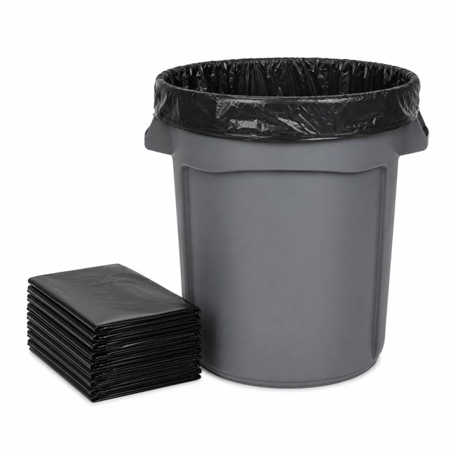 A dark gray plastic trash can with a black plastic liner inside, shown next to a stack of folded black liners on a white background.