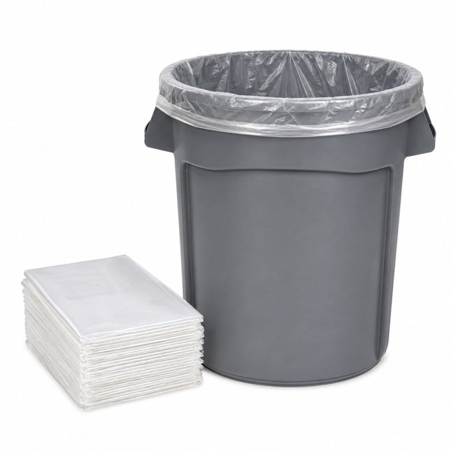 A dark gray plastic trash can with a clear plastic liner inside, shown next to a stack of clear plastic bag liners on a white background.