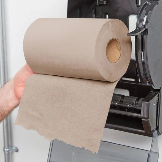 A hand holding a roll of brown paper towels as they are being dispensed from a black countertop paper towel dispenser.